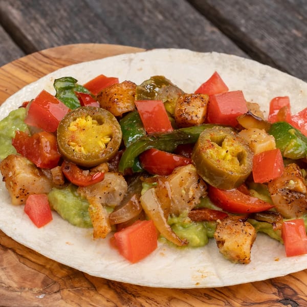 Burrito Mundo's chicken fajita taco with guacamole, peppers, tomatoes, and jalapeños on a wooden board.