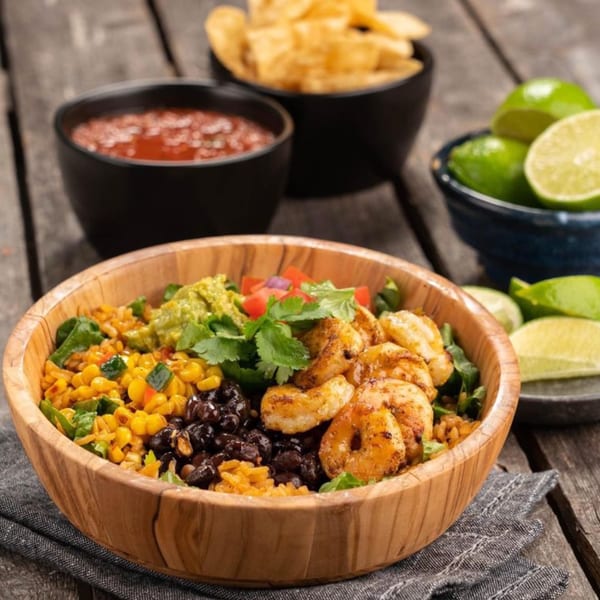 Burrito Mundo shrimp bowl with rice, corn, black beans, guacamole, and cilantro, with salsa, chips, and limes.