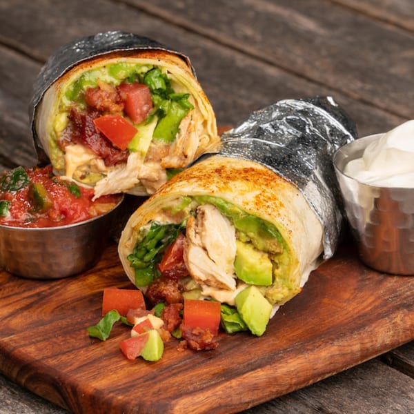 Two Burrito Mundo burritos, one cut in half, filled with chicken, avocado, bacon, and tomatoes.