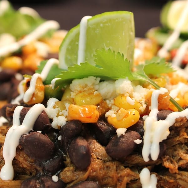 Close-up of Mexican food with black beans, corn, cheese, cilantro, lime, and crema.
